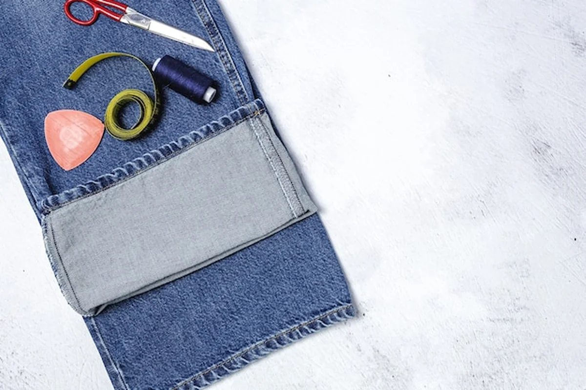 Naprawa odzieży - szycie dziur w niebieskich dżinsach z akcesoriami do szycia