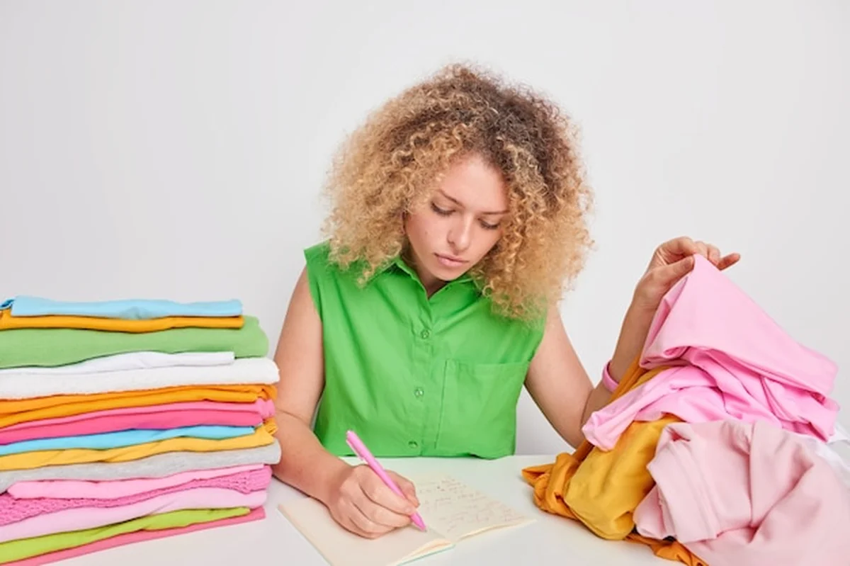 Młoda kobieta z kręconymi włosami pisząca w pamiętniku, sortująca ubrania przy stole