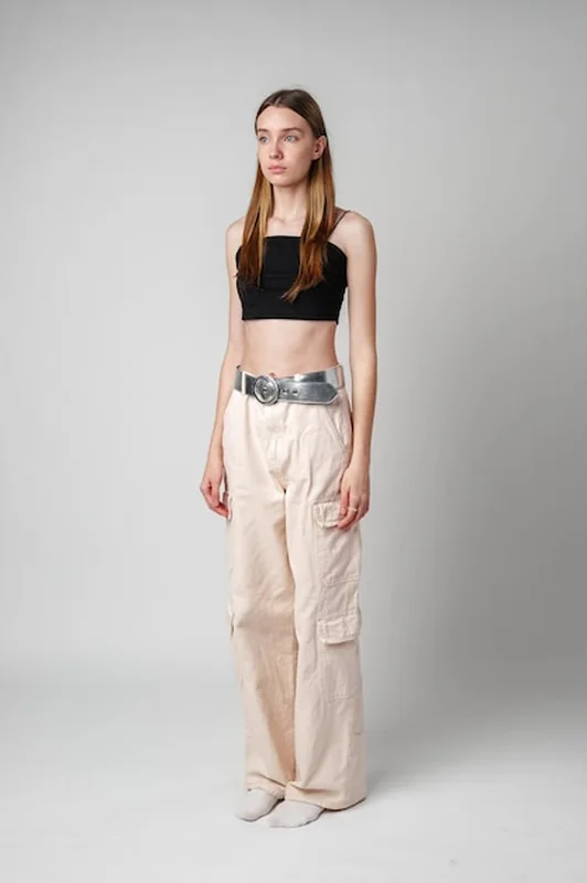 Młoda kobieta w beżowych spodniach i czarnym topie przed białą ścianą