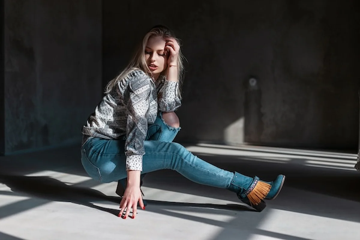 Młoda kobieta w jeansach, zielonych kowbojskich butach i koszuli, siedząca w pokoju ze światłem słonecznym