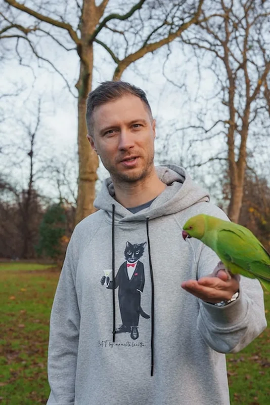 Mężczyzna w szarym kapturze z papugą w parku zimowym w Londynie
