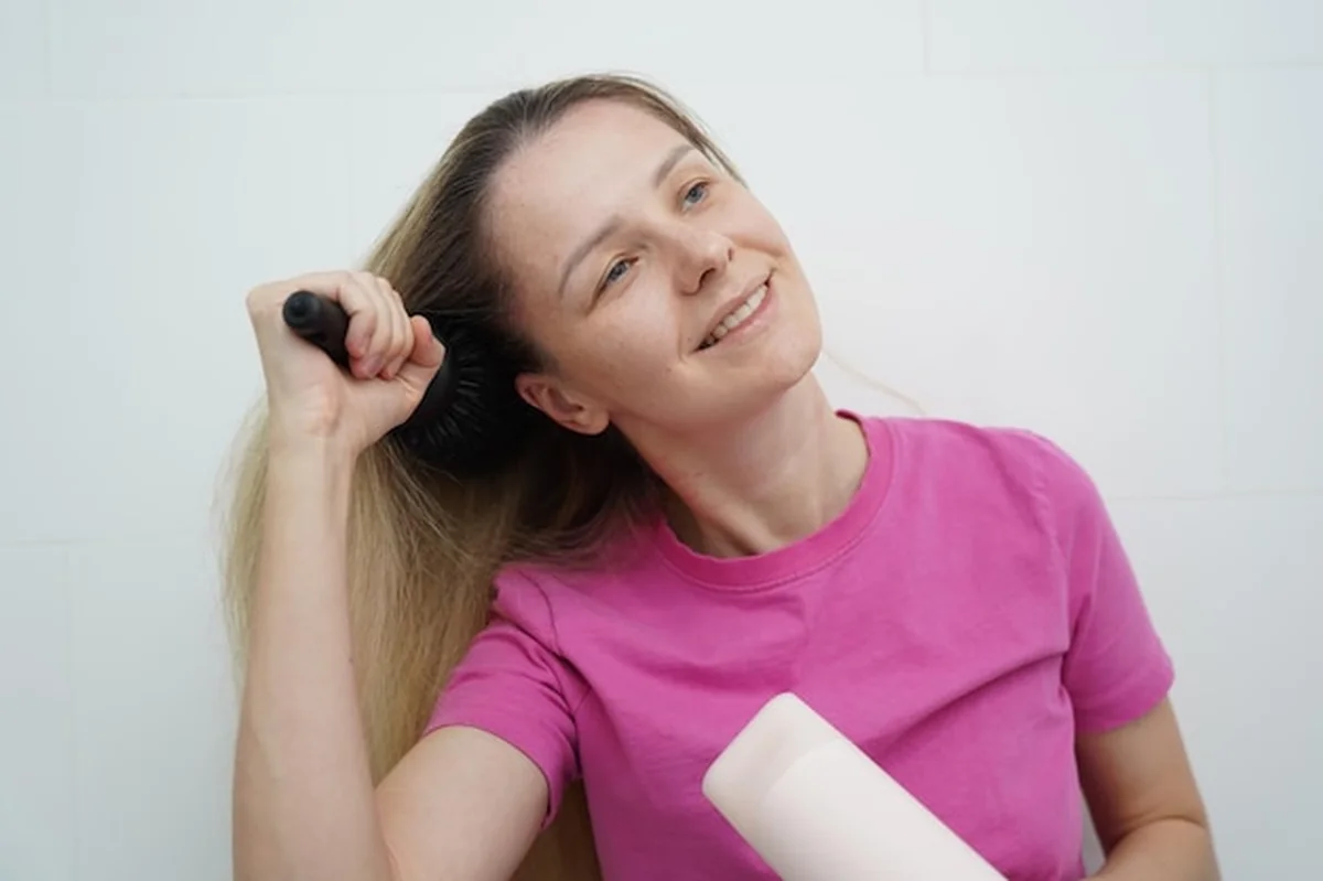 Kobieta suszy włosy suszarką i szczotką w łazience