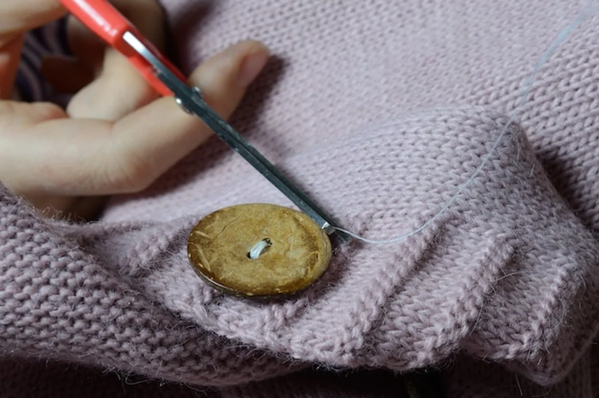 Ręce przyszywają drewniany guzik do kurtki