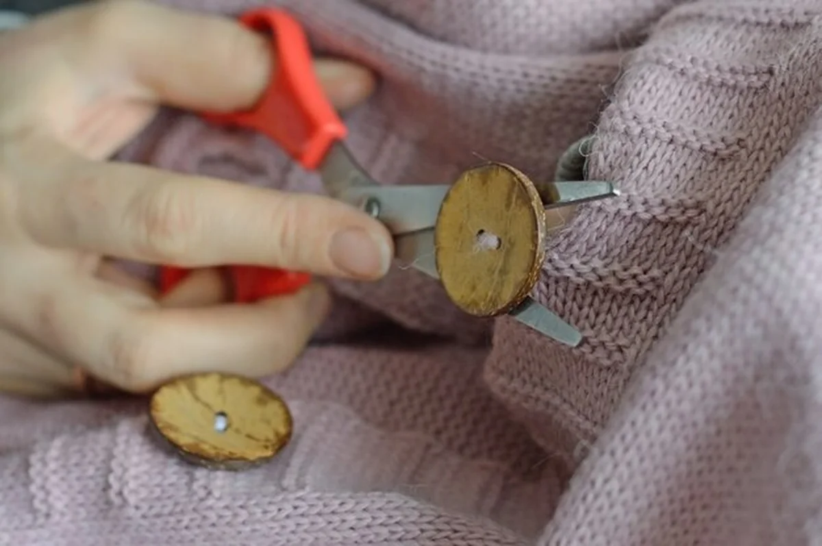 Ręce pracownic przyszywają drewniany guzik do kurtki