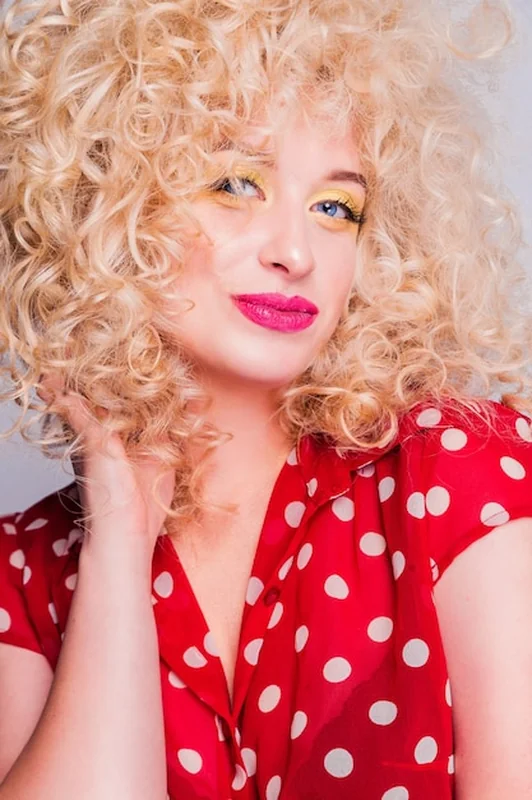 Blondynka z fryzurą mullet, jasnym makijażem i czerwoną bluzką w kropki