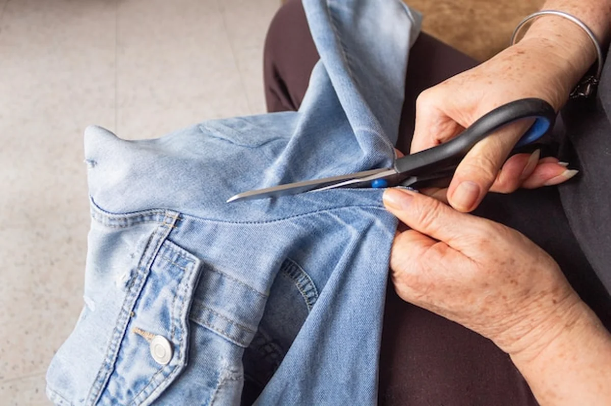 Kobieta używająca nożyczek do cięcia rękawa kurtki dżinsowej