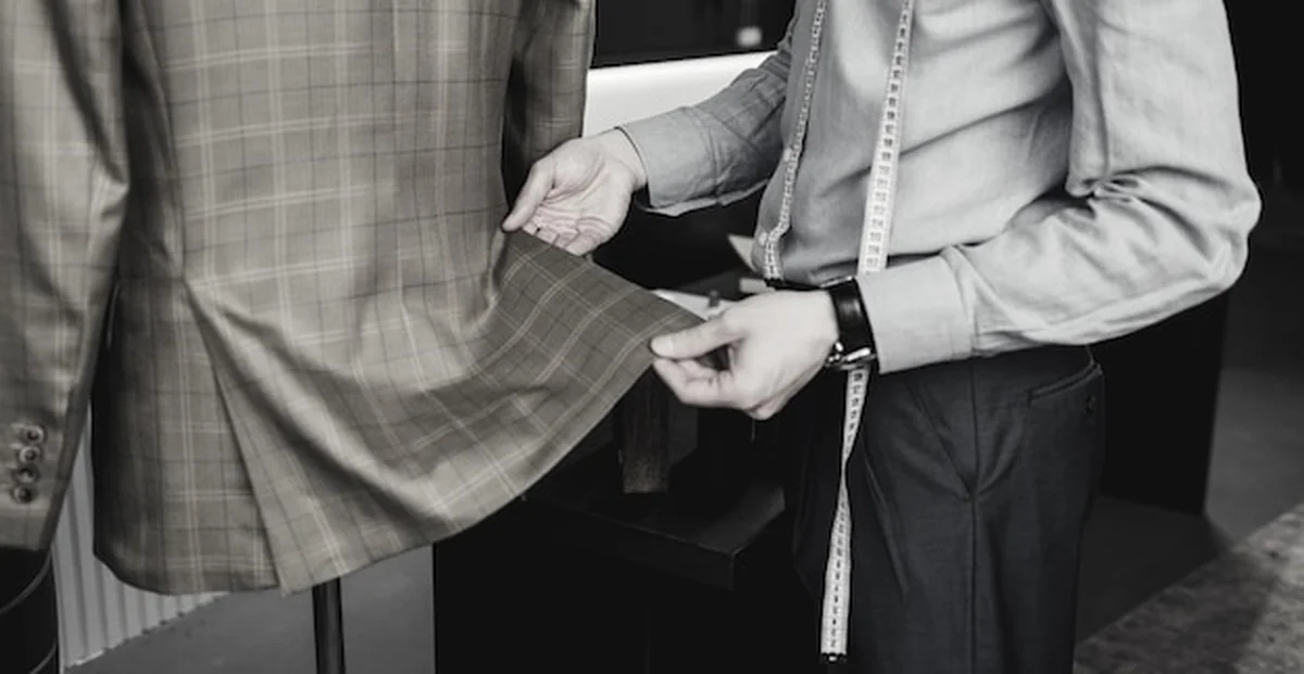 Krawiec z miarką w warsztacie sprawdza gotowy garnitur