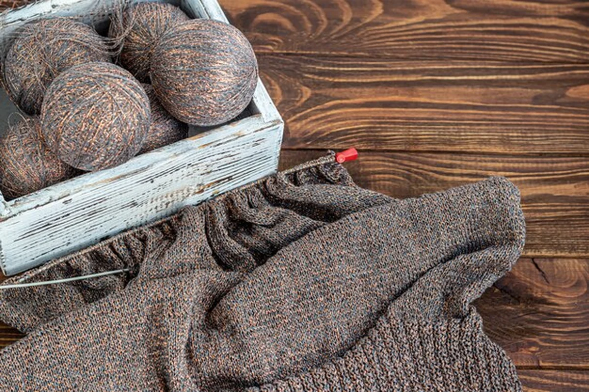 Metalowe igły dziewiarskie i wełniane nici na drewnianym tle